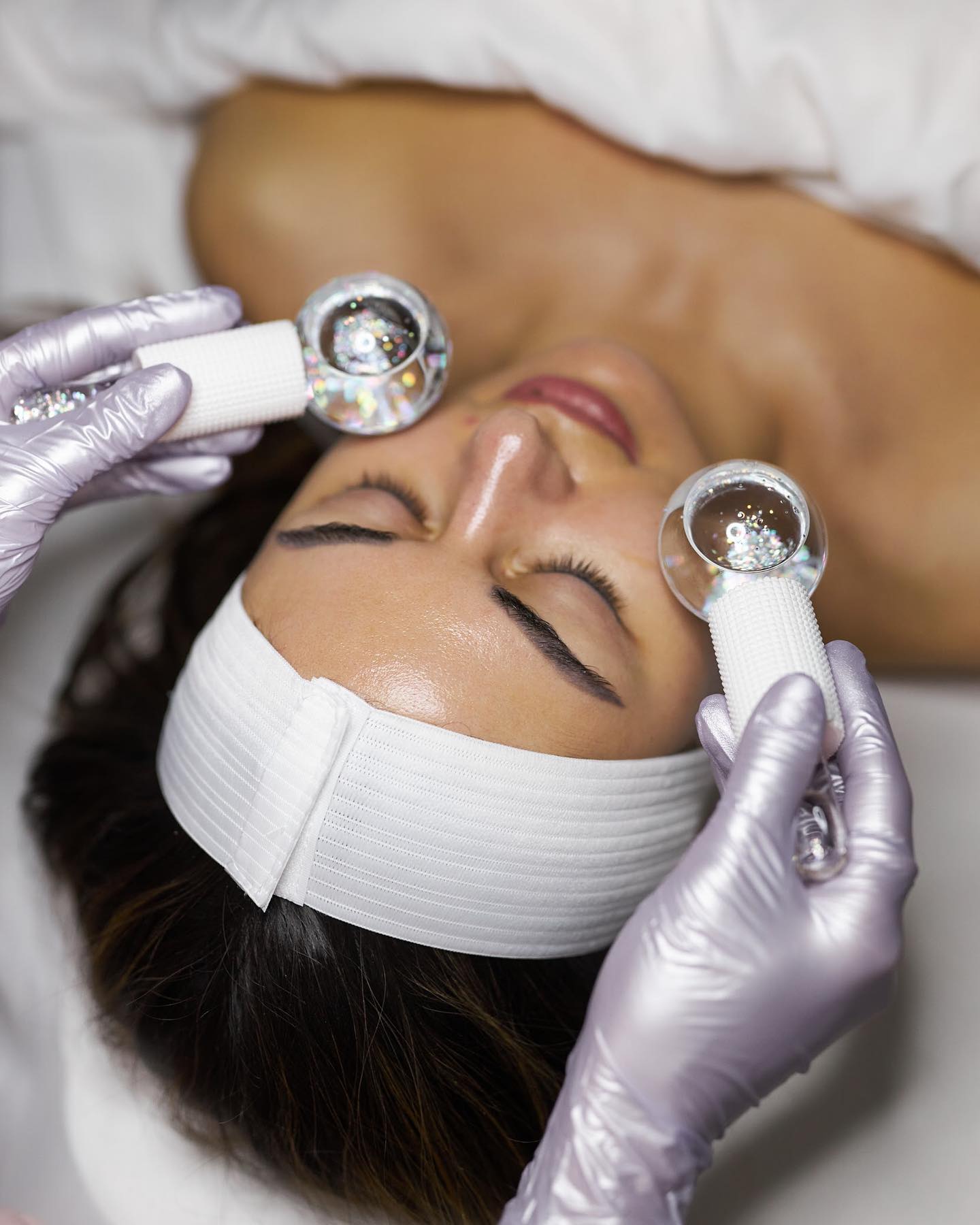 Gloved hands hold ice globes to a person's face.
