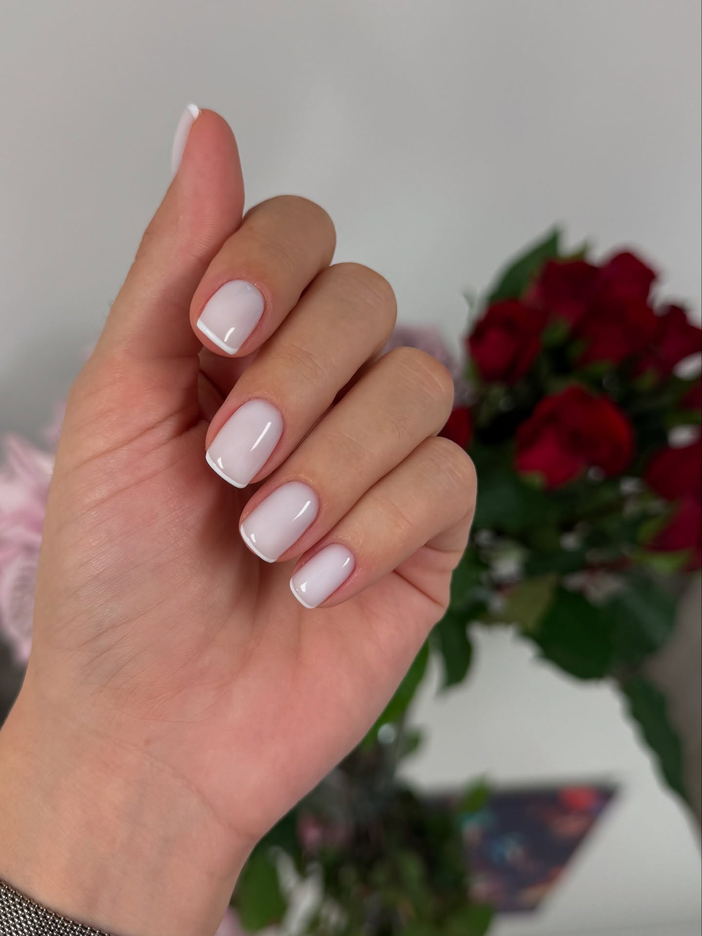 Hand with clean white French tip nails and red roses.