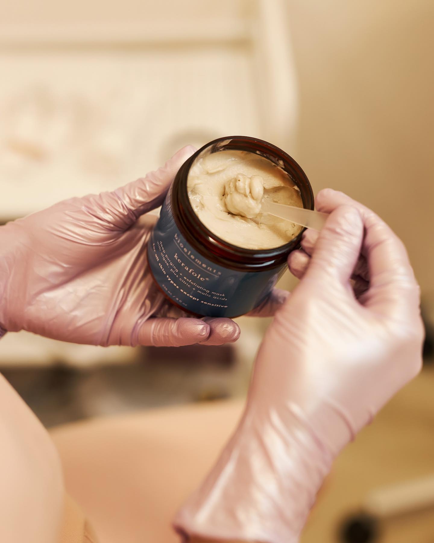 Gloves scooping cream from a jar labeled "bioelements kerafole".
