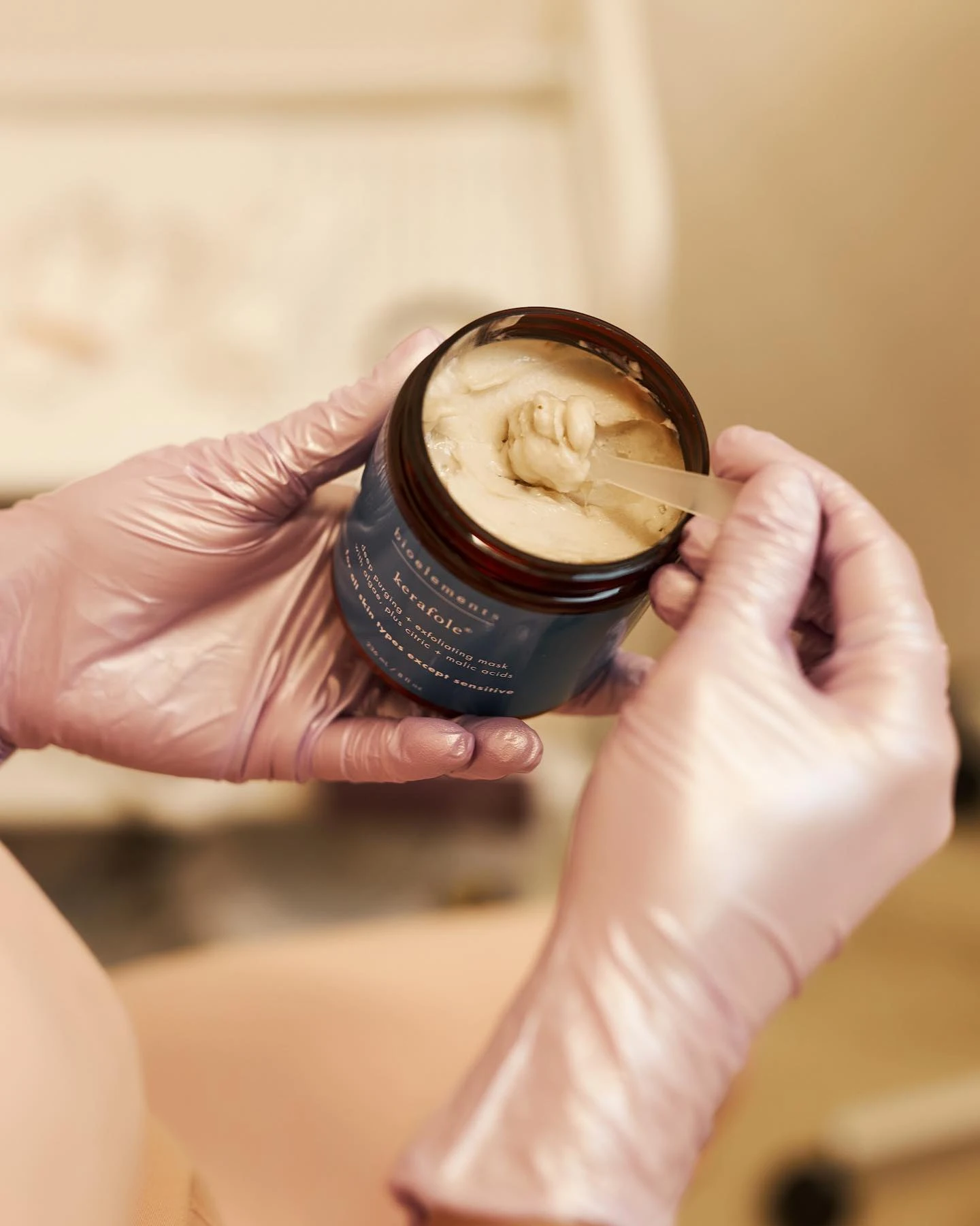 Gloves scooping cream from a jar labeled "bioelements kerafole".