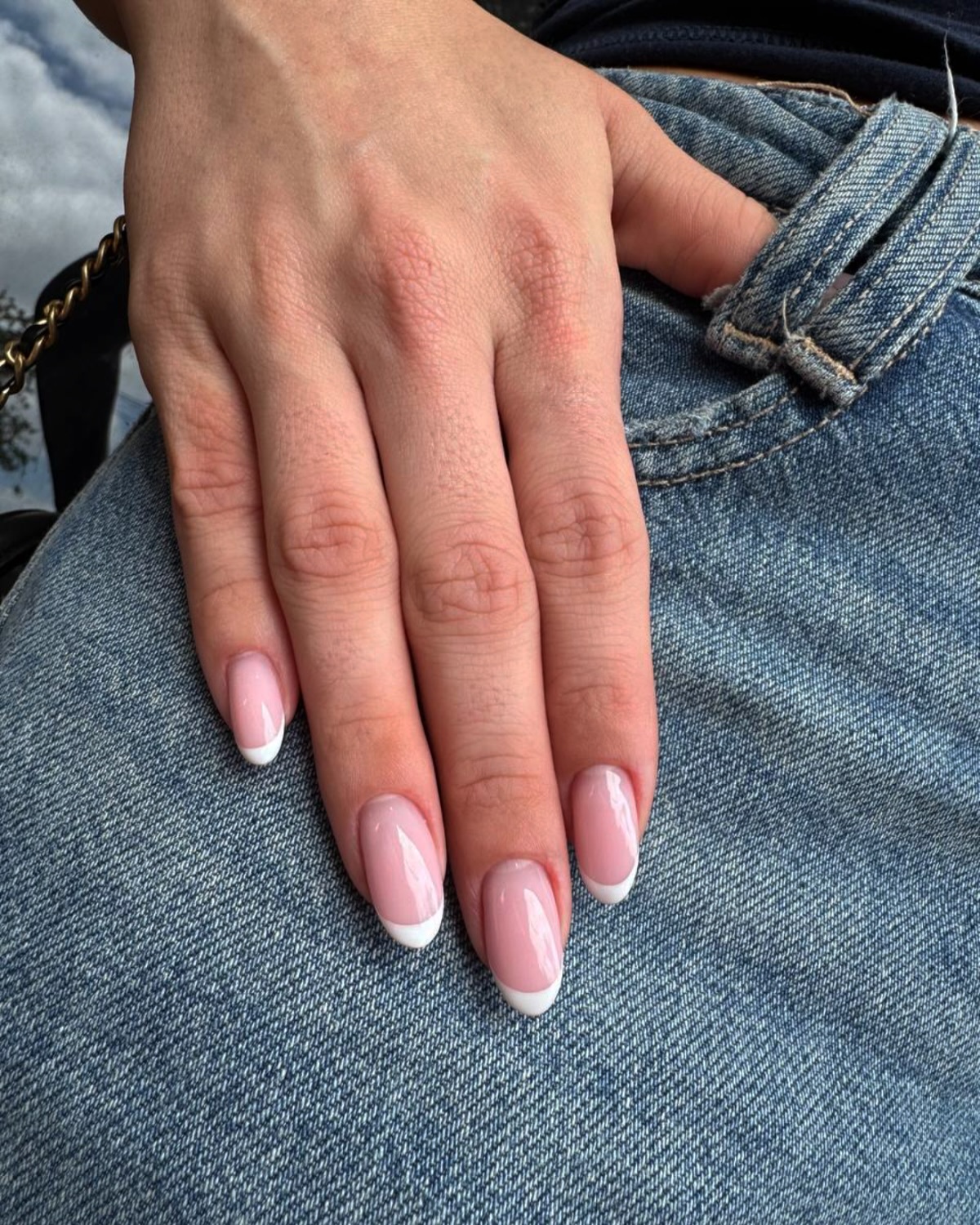 Hand with pink and white French tip nails on denim.