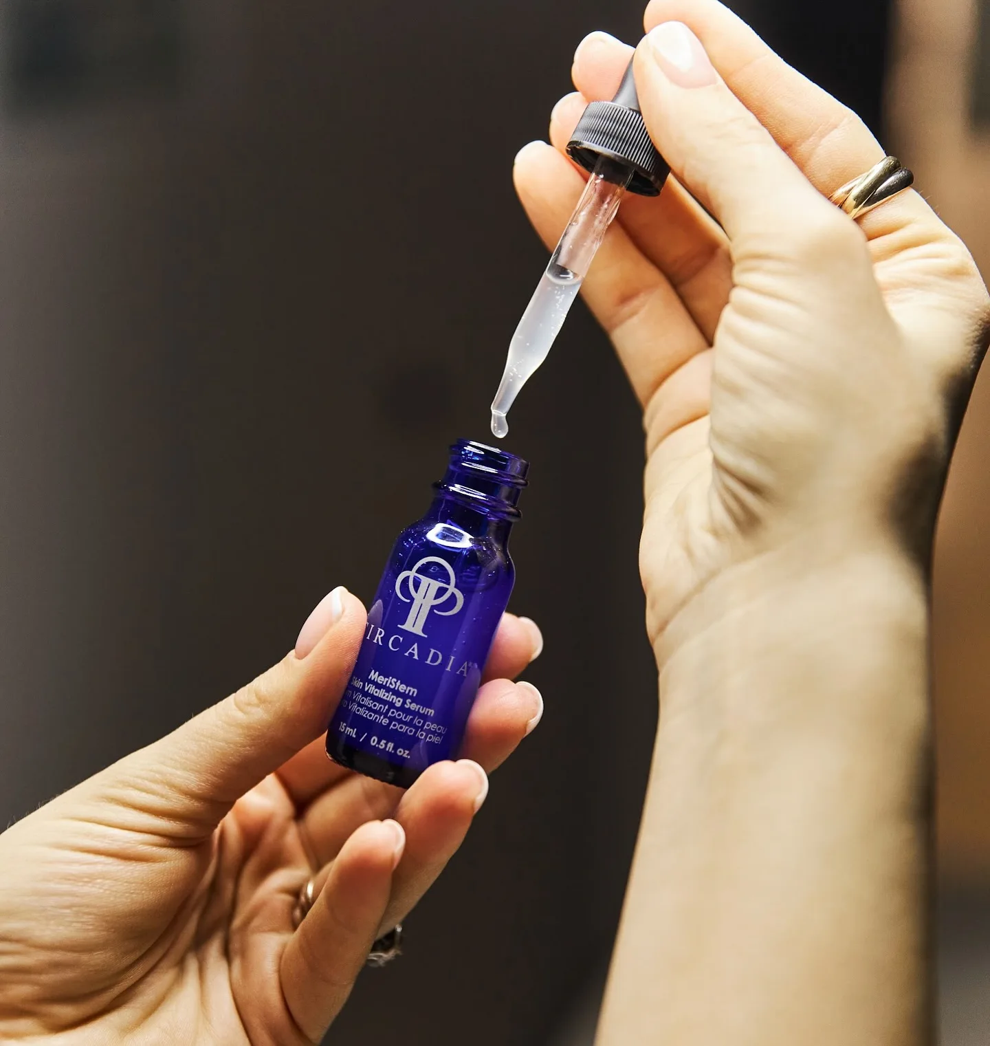 nn Hands holding a dropper and a small blue bottle with serum.