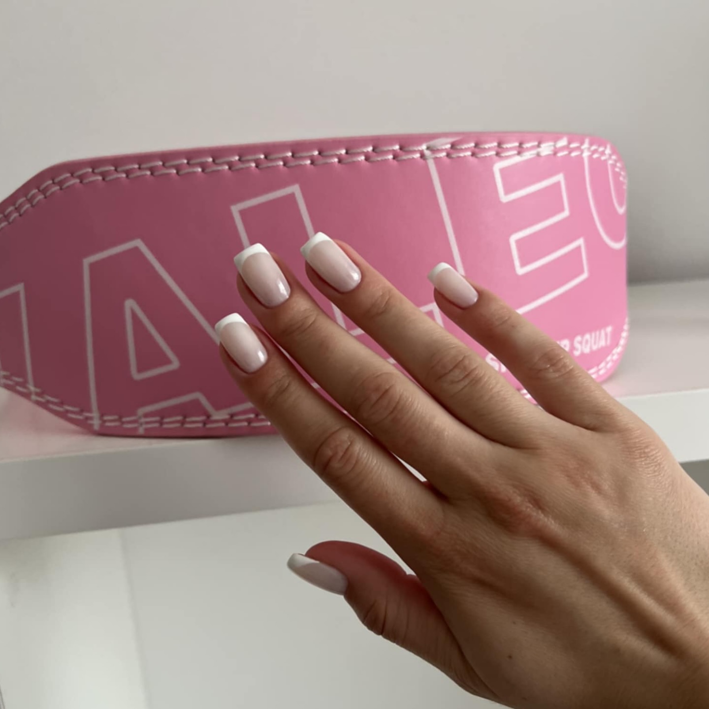 Hand with french manicure in front of pink object with white text.