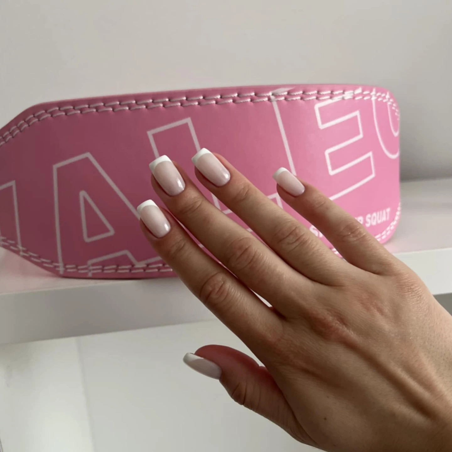 Hand with french manicure in front of pink object with white text.