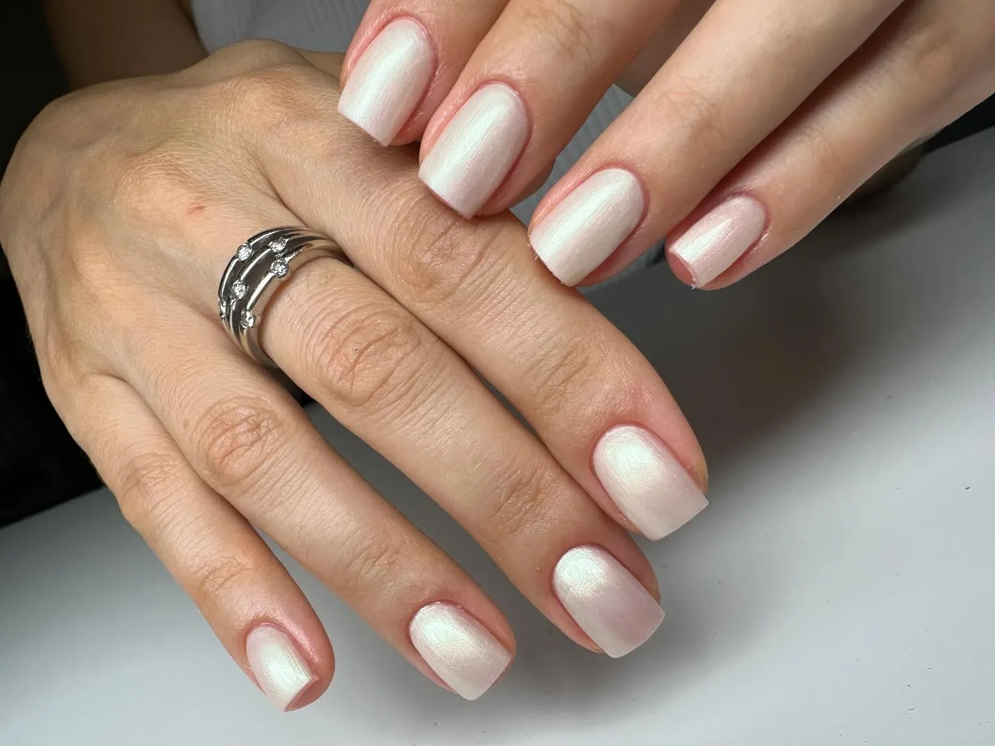 Hands with pearlescent nails and a diamond ring.