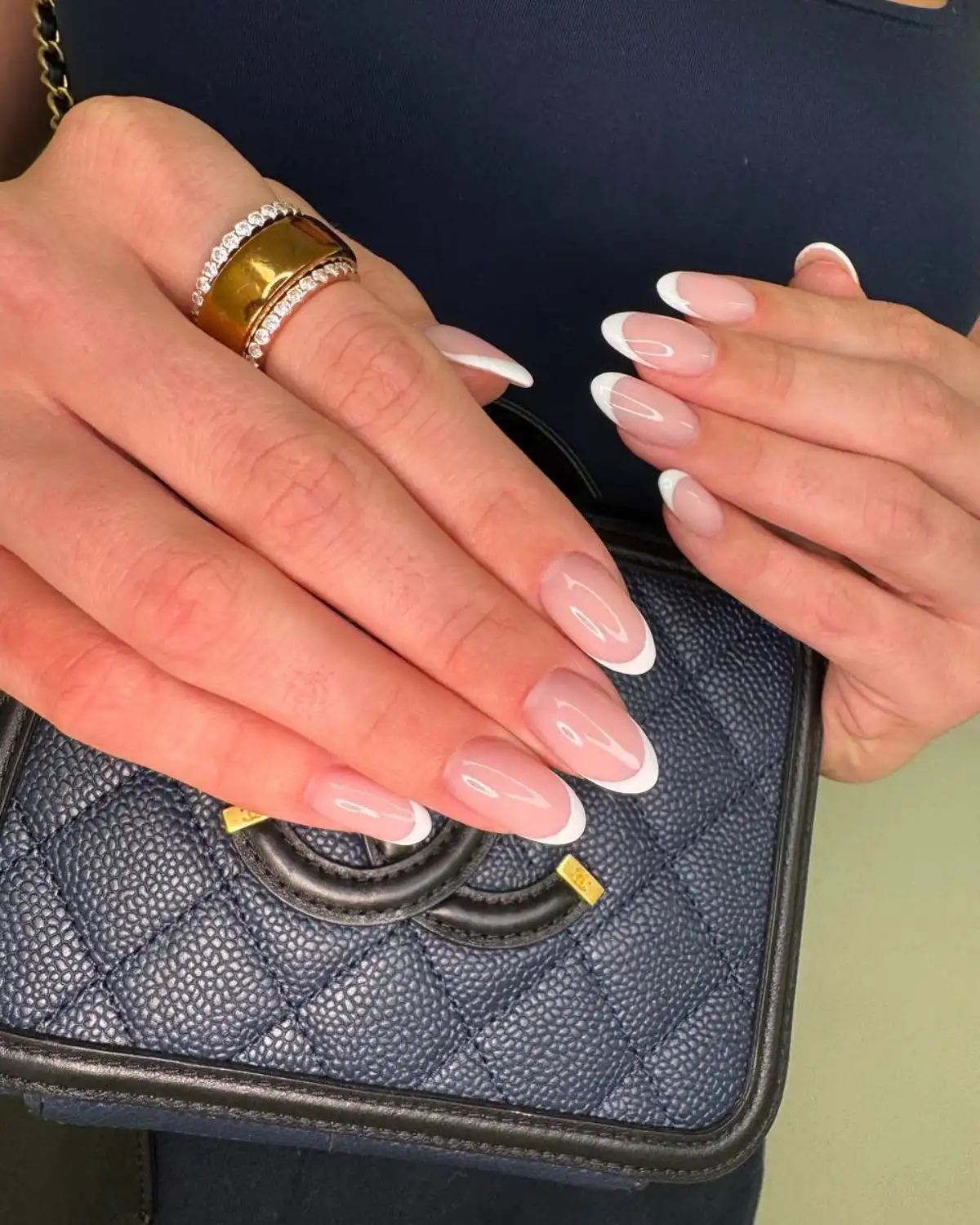 French tip oval nails and a gold ring on a quilted purse.