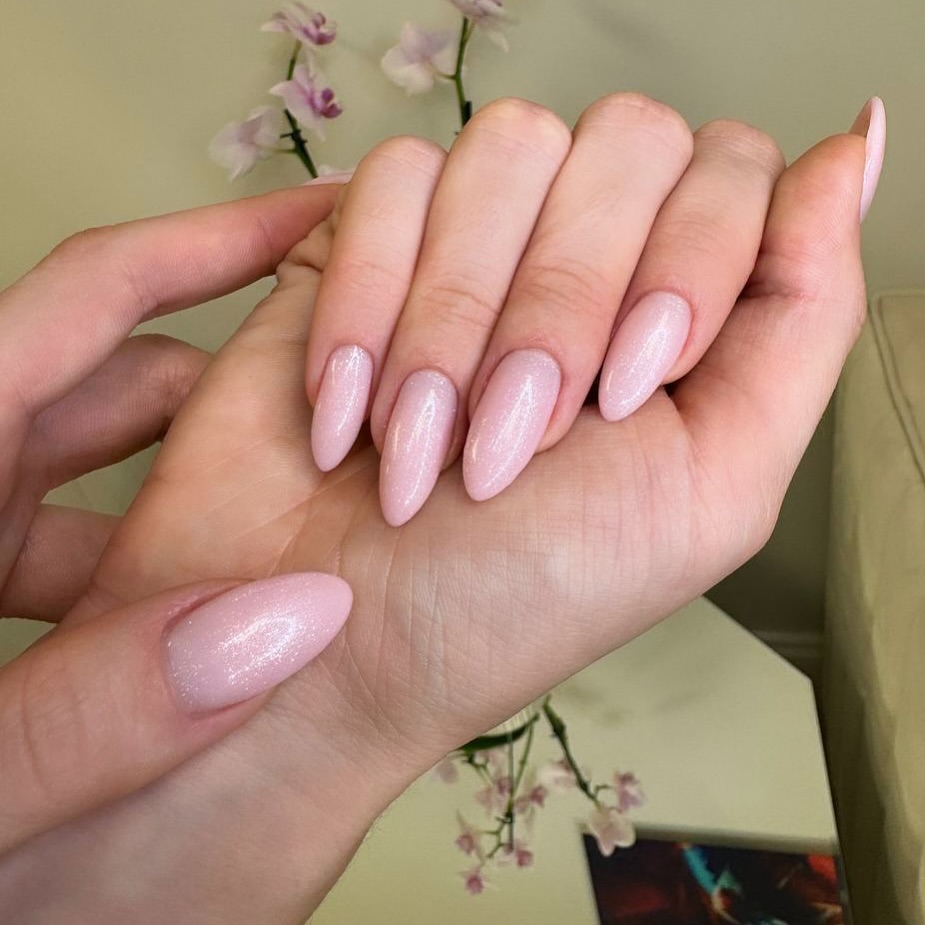 Close-up of hands with light pink glitter almond-shaped nails.