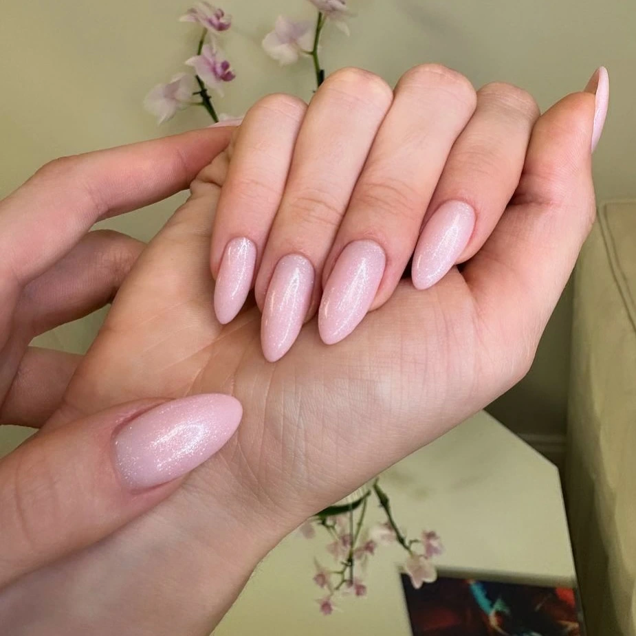 Close-up of hands with light pink glitter almond-shaped nails.