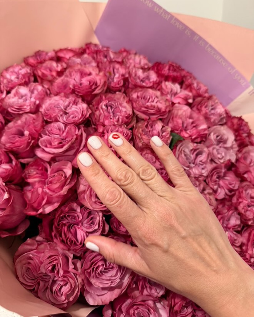 Hand with white nails and red lips design on pink roses.