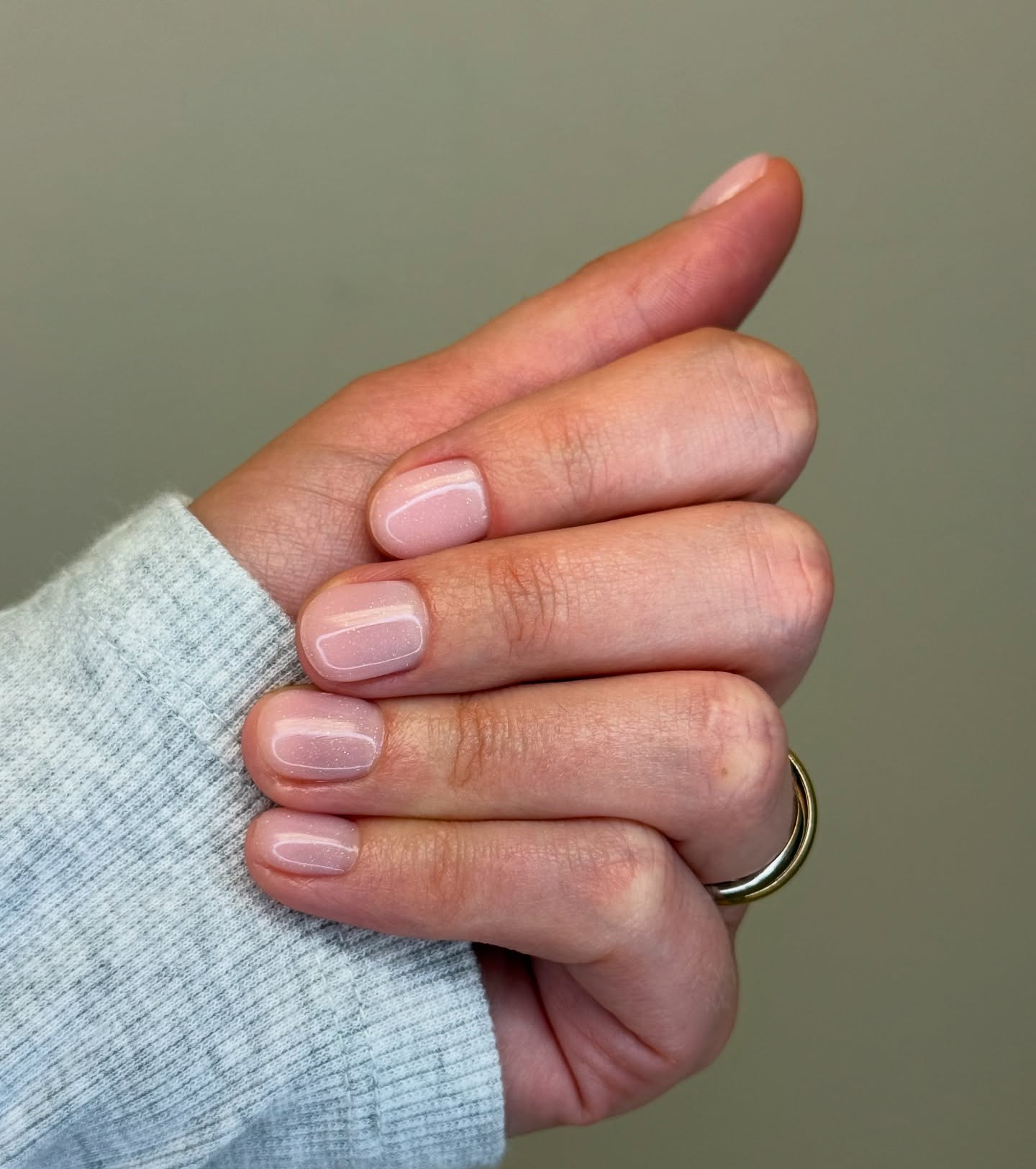 Hand with light pink glitter nails and a gold ring.