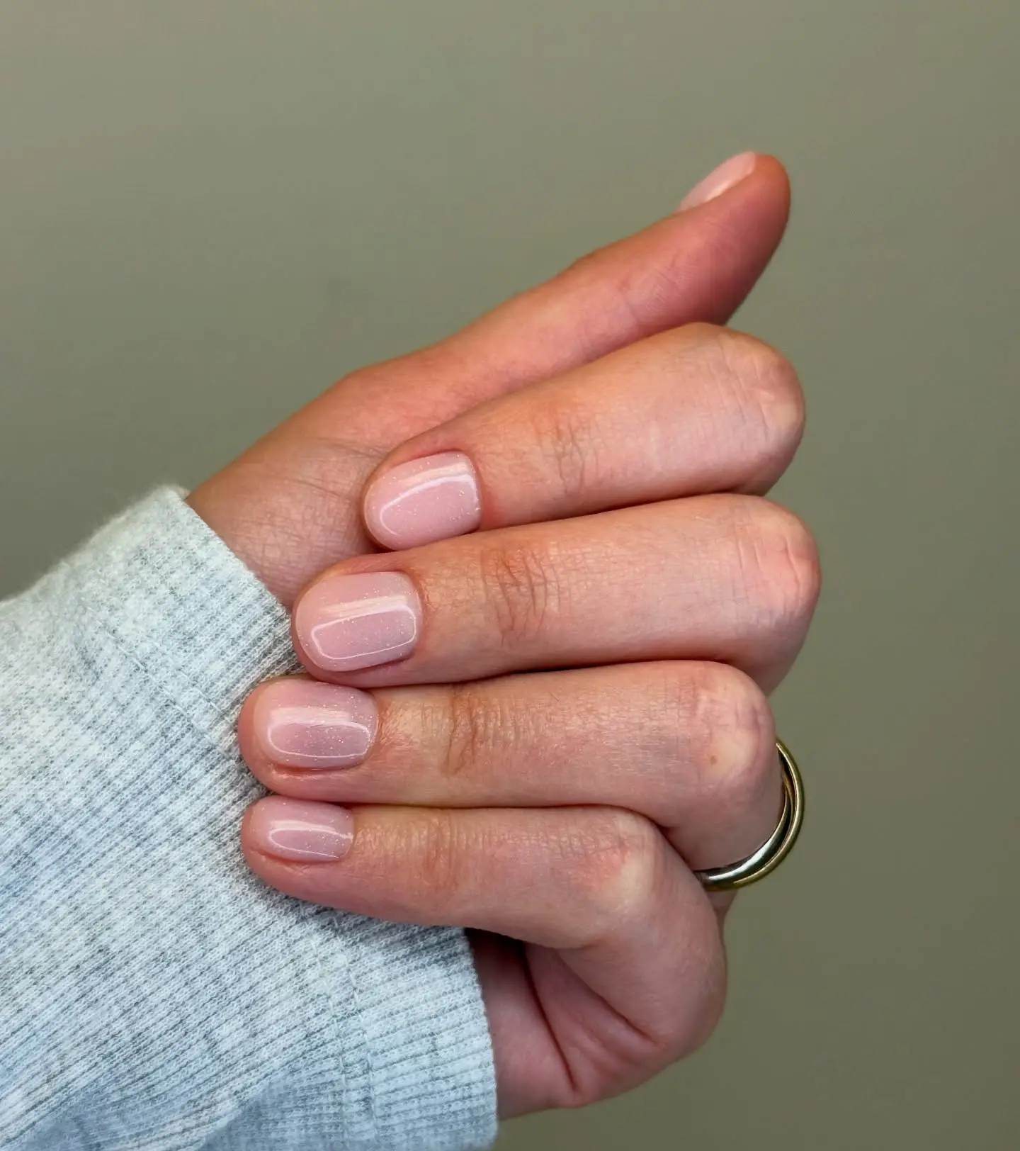 Hand with light pink glitter nails and a gold ring.