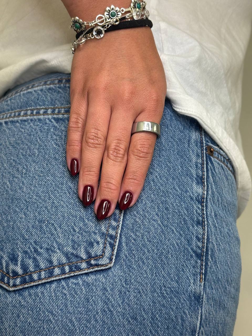 Hand with dark red nails and silver ring on blue jeans.