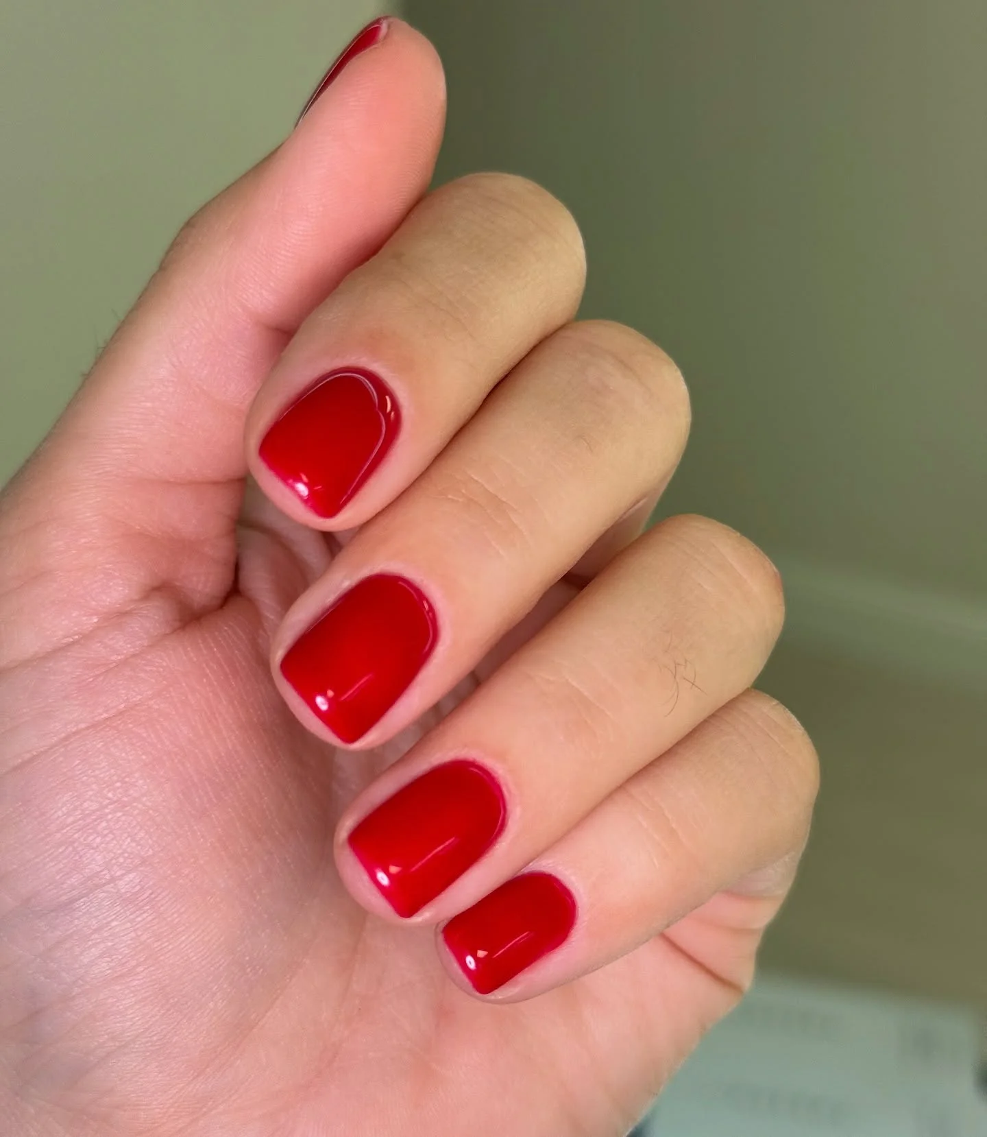 Hand with bright red polished nails against a pale green background.