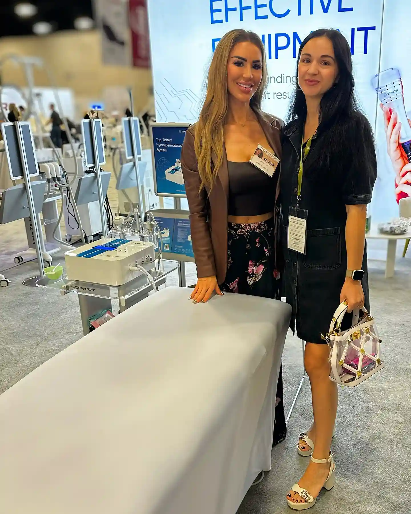 Two women stand by a medical treatment table and equipment.