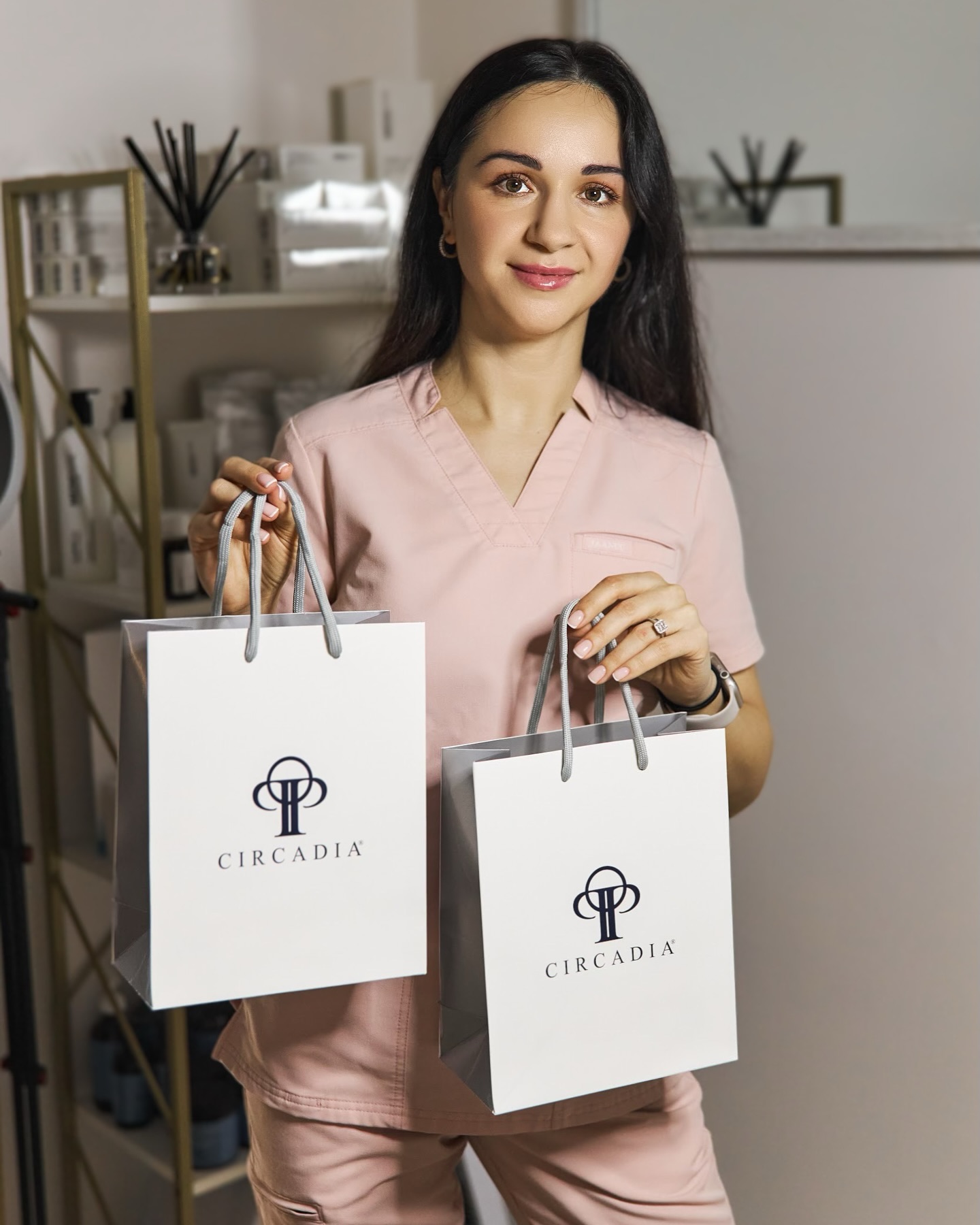 Woman in pink scrubs holds two white shopping bags with "CIRCADIA" logo.
