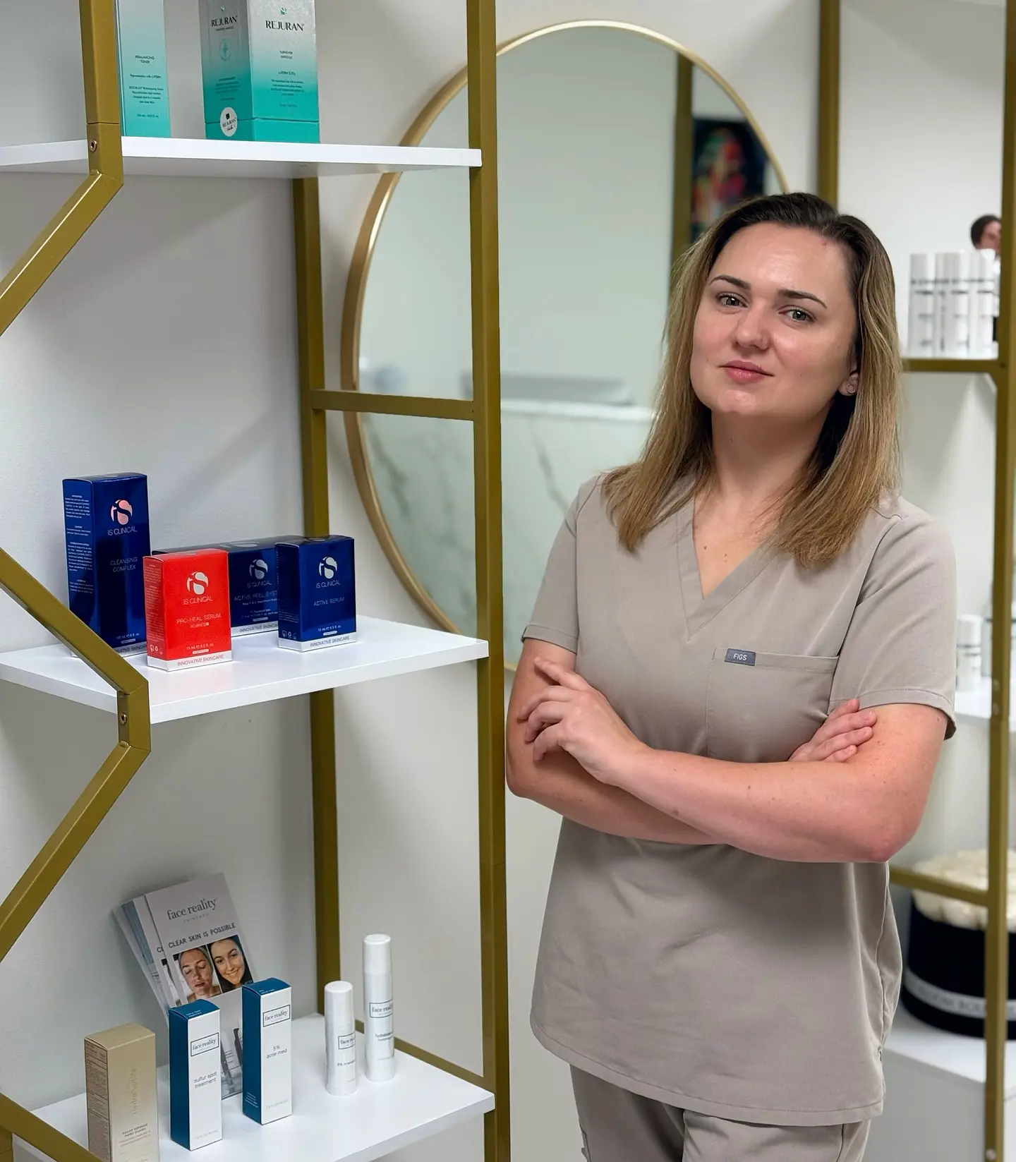 nn Woman in beige scrubs stands with arms crossed in a spa.